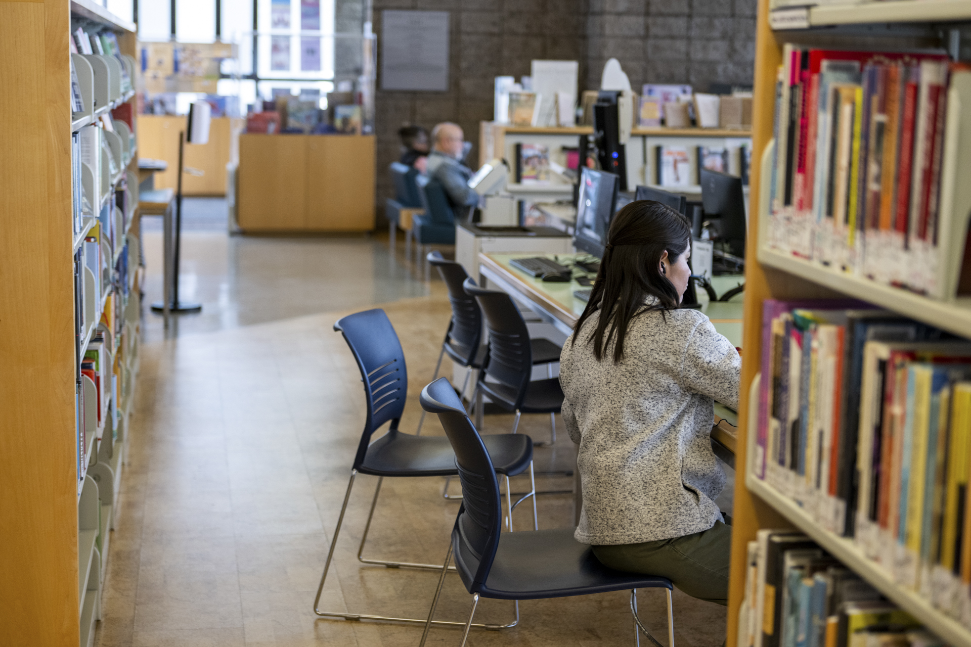 A person in a library with chairs, desks, and bookshelves in the background.